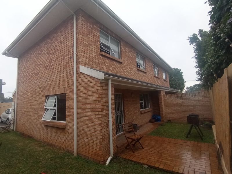 Rear view of a double-storey townhouse featuring a face brick exterior, paved patio area, and enclosed garden space.