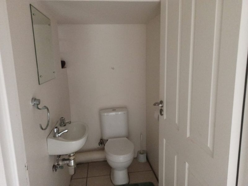 A compact guest bathroom featuring a wall-mounted basin, toilet, and tiled flooring, providing essential utility in a small footprint.