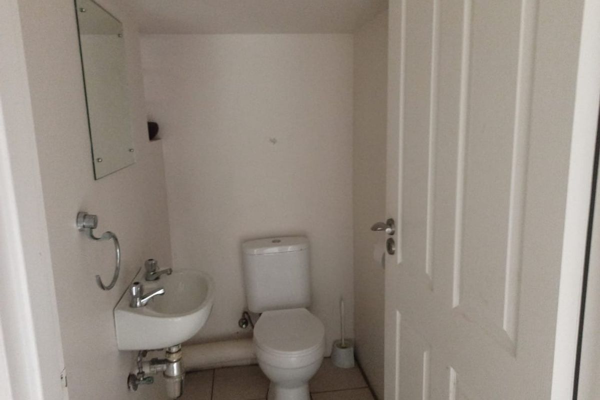 A compact guest bathroom featuring a wall-mounted basin, toilet, and tiled flooring, providing essential utility in a small footprint.