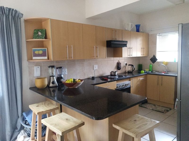 A functional kitchen featuring light wood cabinetry, dark granite countertops, a built-in oven with hob, and a breakfast bar area.