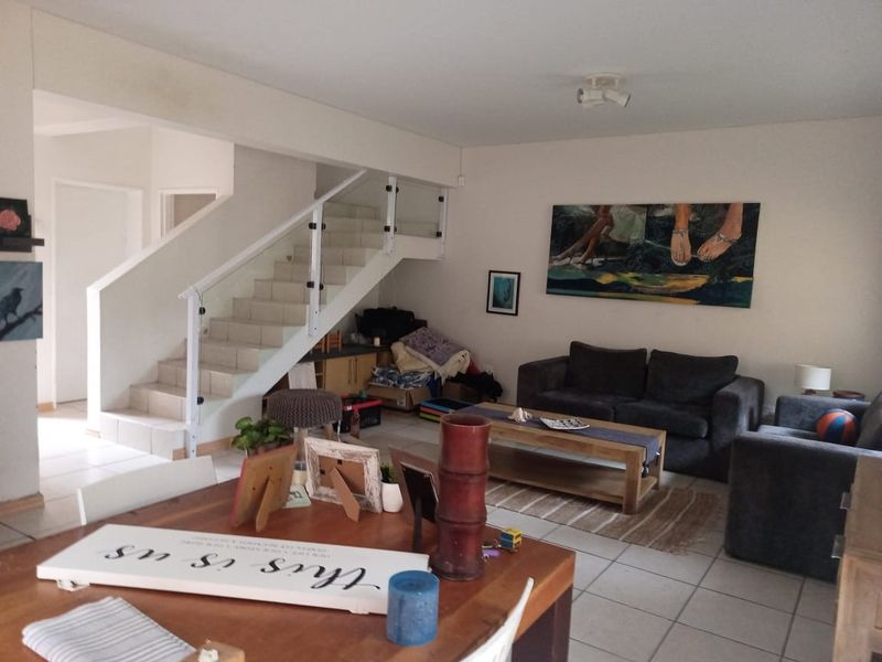 Open plan living area featuring tiled flooring and a modern staircase with a glass balustrade, providing a functional and connected layout.