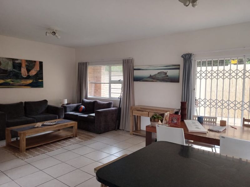 Open plan living and dining area featuring tiled flooring, large windows, and a security gate leading to the outdoor space.