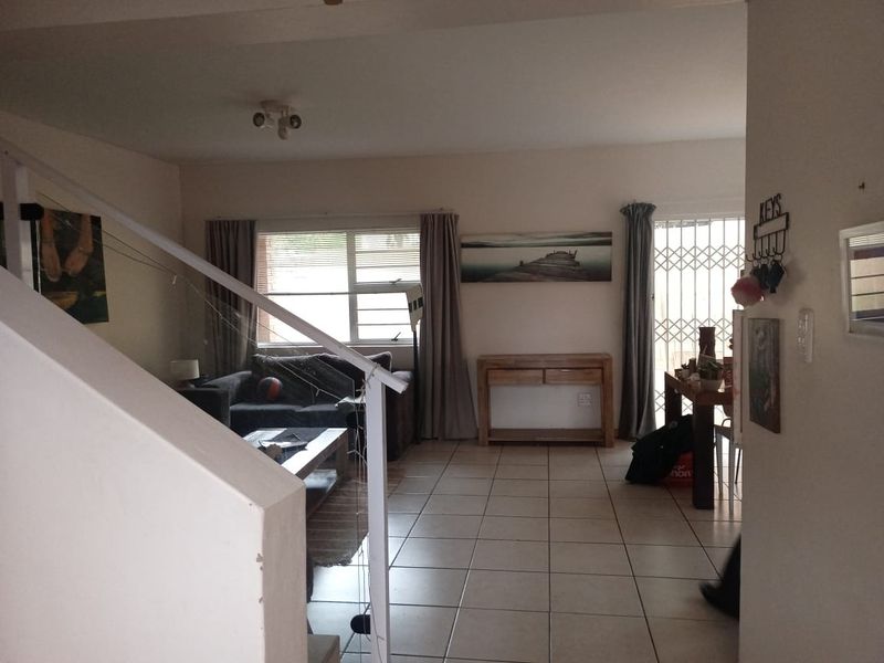 Open plan living area featuring tiled flooring, a staircase with metal railing, and access to an outdoor area through a security gate.