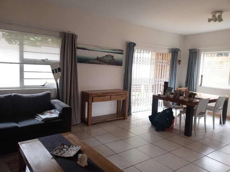 Open-plan living and dining area featuring tiled flooring, large windows, and a sliding door with security gate providing access to the exterior.