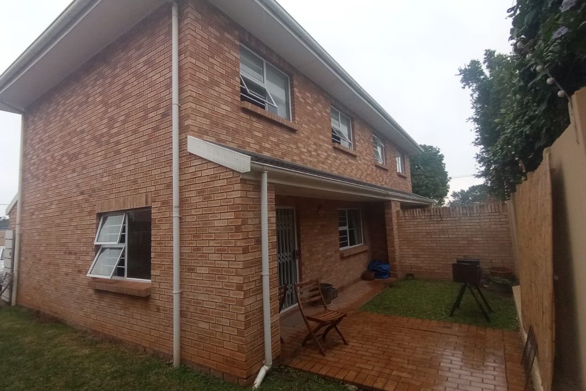 Rear view of a two-story face brick townhouse featuring a paved patio area and a small private garden space.