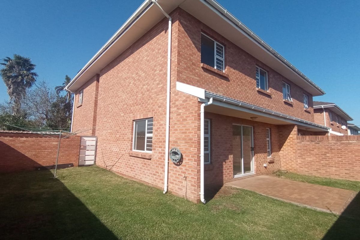 Rear view of the townhouse featuring a brick facade, paved patio area, and a private lawn enclosed by a brick boundary wall.