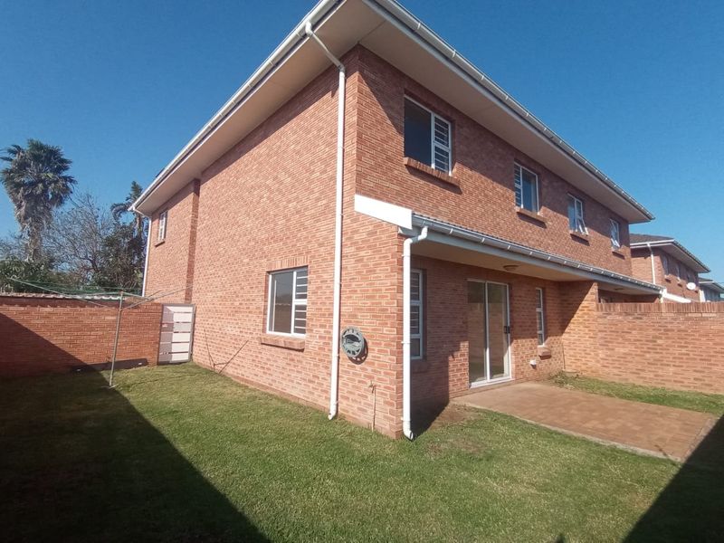Rear view of the townhouse featuring a brick facade, paved patio area, and a private lawn enclosed by a brick boundary wall.