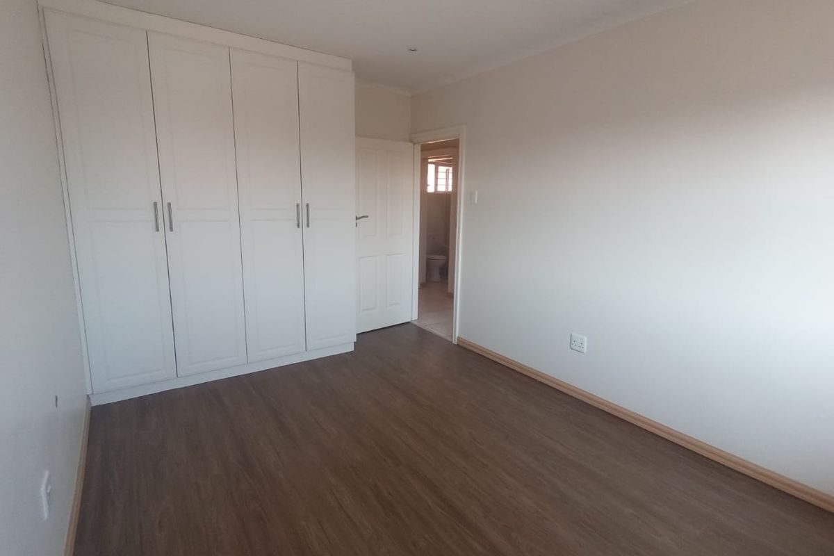 A clean, empty bedroom featuring modern laminate flooring, built-in white cupboards, and neutral walls, offering a versatile space ready for personalization.