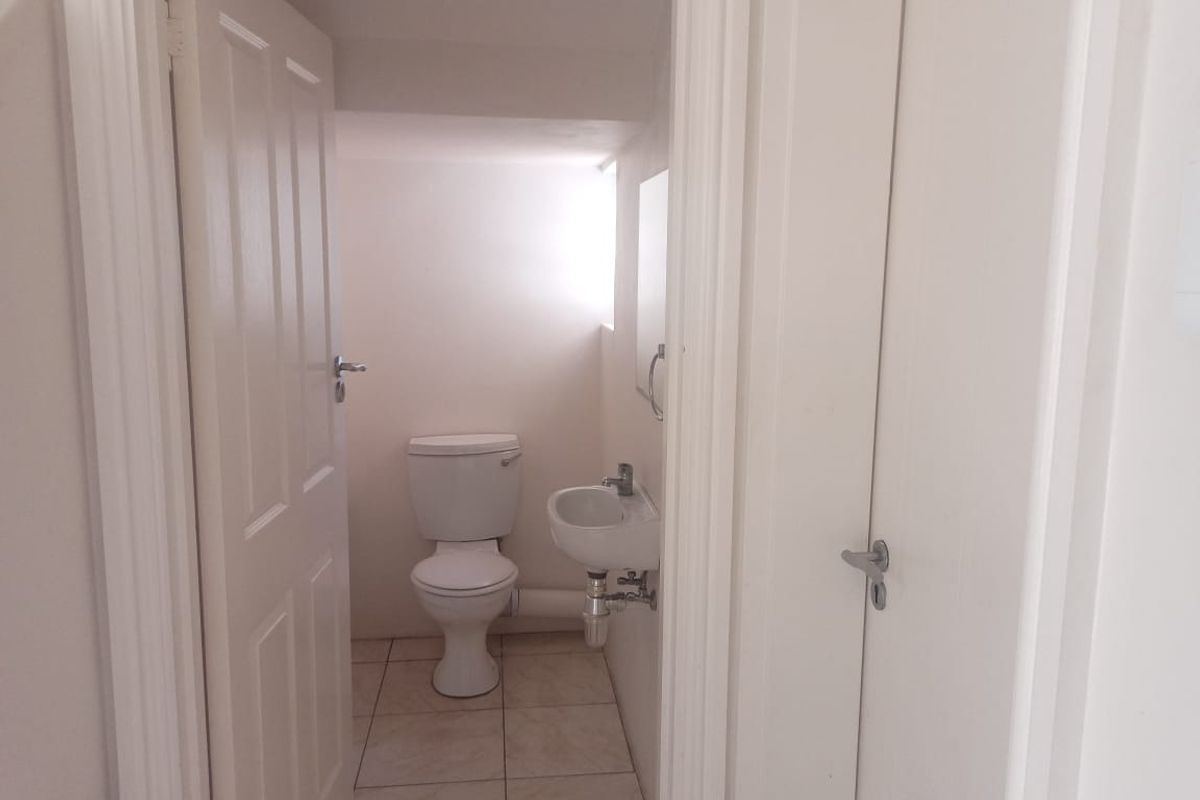 A compact guest bathroom featuring a toilet, wall-mounted basin, and tiled flooring, accessible via a hallway door.