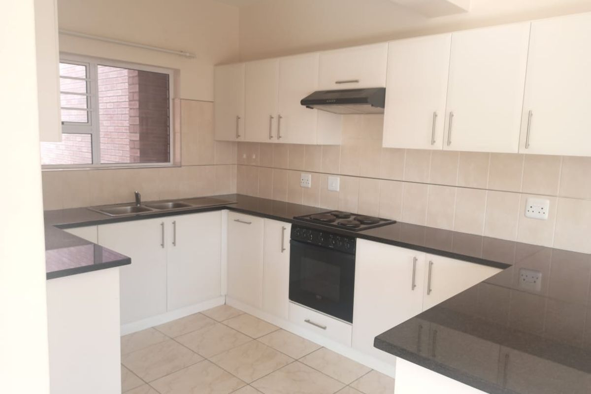 A clean, functional kitchen featuring white cabinetry, dark granite countertops, built-in oven, hob, extractor fan, and neutral tiled flooring.