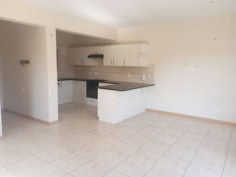 An open-plan kitchen and living area featuring tiled flooring, built-in cabinetry with granite countertops, and an integrated oven with extractor fan.