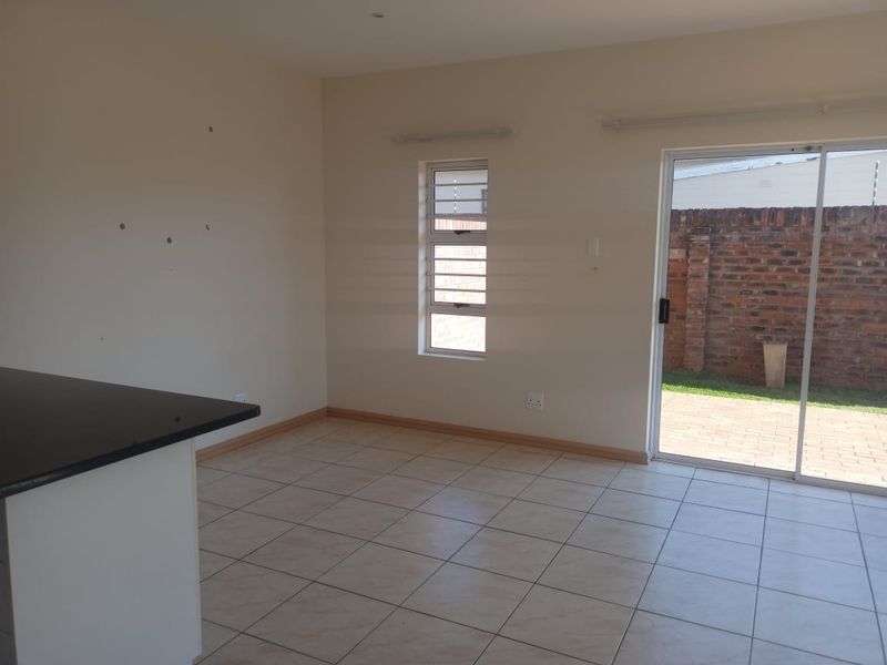 An empty open-plan living area featuring tiled floors, a kitchen island with a granite countertop, and sliding glass doors leading to a paved patio.