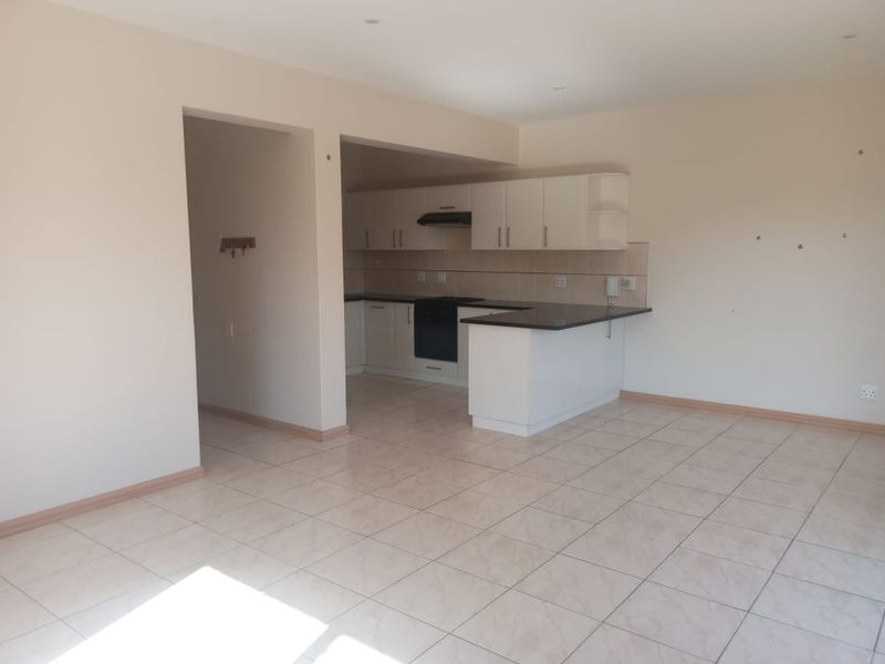 An open-plan living and kitchen area featuring tiled flooring, built-in cabinetry, and a breakfast counter, presenting a clean, vacant space ready for personalization.