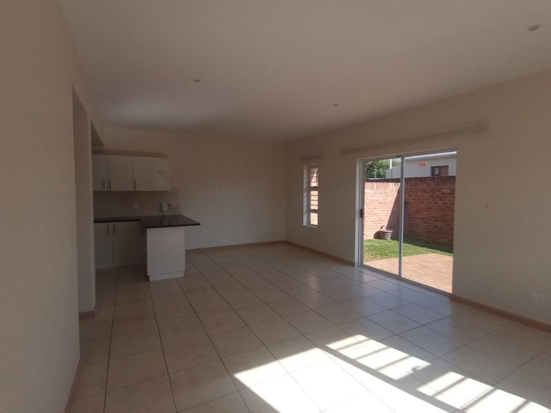 Spacious open-plan living area featuring tiled floors, a compact kitchen with granite countertops, and direct access to a private rear garden through sliding doors.