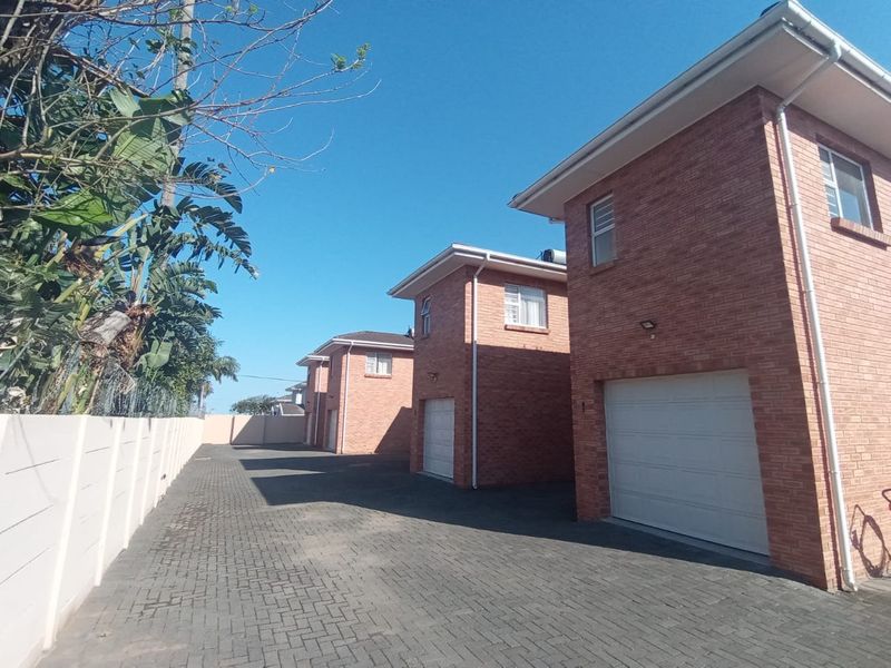 Exterior view of a townhouse complex featuring face brick facades, paved driveway access, and individual sectional garage doors.