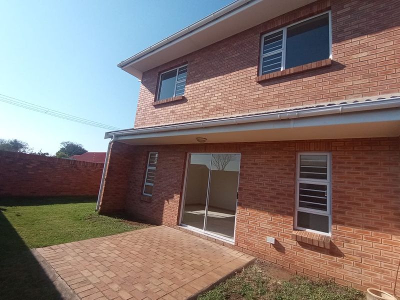 Rear view of a double-storey townhouse featuring a face-brick facade, a paved patio area, and a sliding glass door leading to the interior.