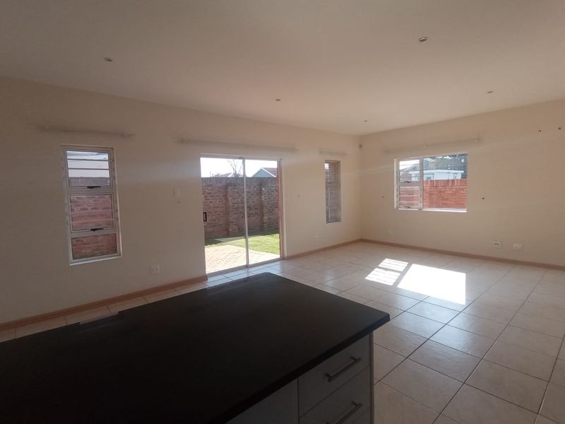 Spacious open-plan living area featuring tiled floors, recessed lighting, and a kitchen island, with direct access to the rear garden through a sliding door.