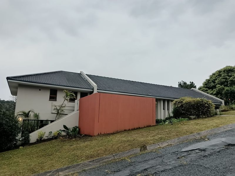 Front elevation of a single-story house featuring a tiled roof, concrete driveway, and a prominent painted retaining wall.