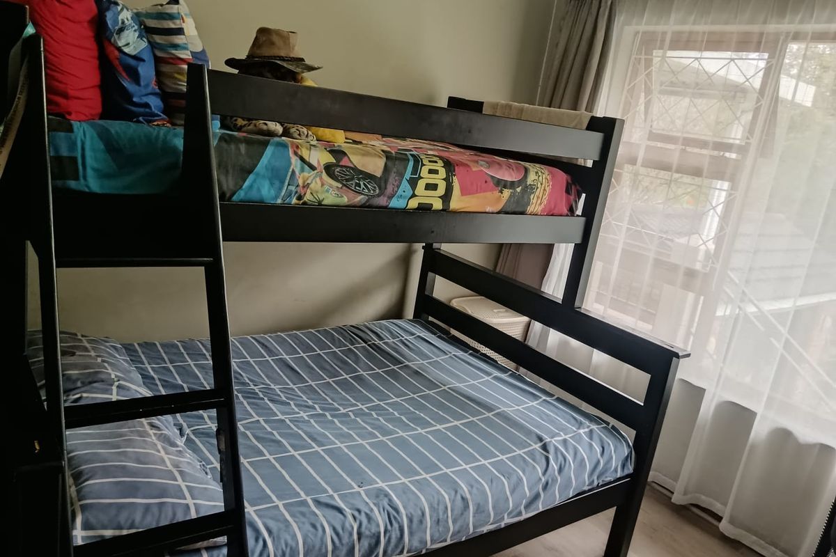 A functional bedroom featuring laminate flooring and a window fitted with security bars, providing natural light and a view of the exterior.