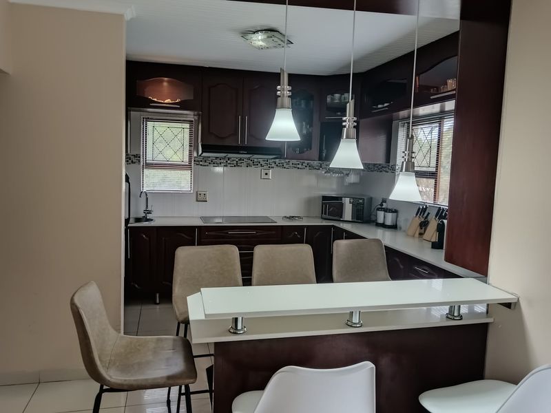 A functional kitchen featuring dark wood cabinetry, a breakfast bar with pendant lighting, and a tiled backsplash, offering a practical layout for daily use.