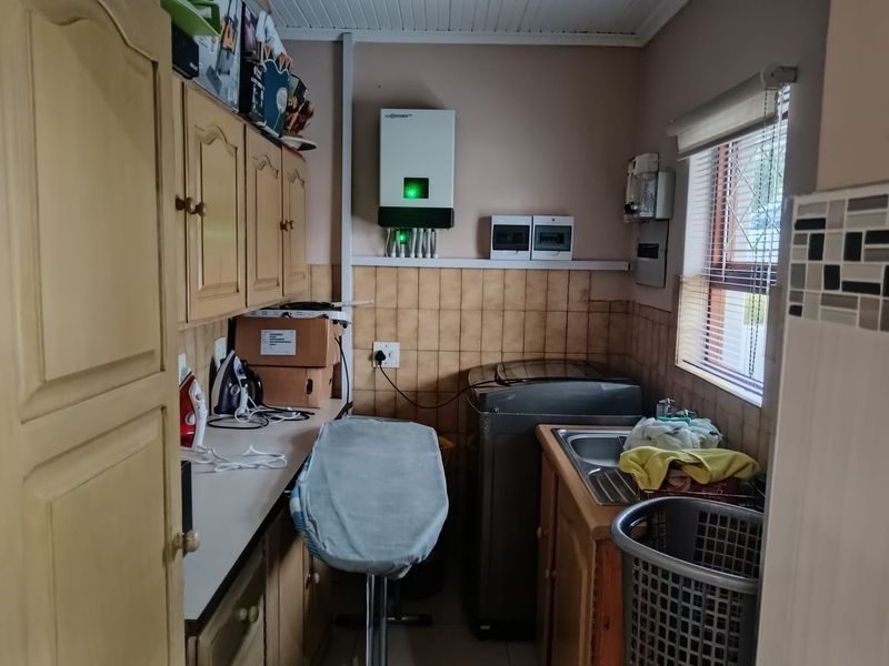 Functional laundry room featuring built-in wooden cabinetry, a stainless steel sink, tiled splashback, and a wall-mounted inverter system.