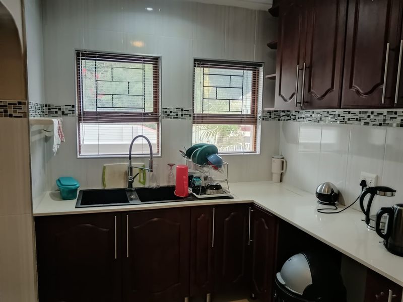 A functional kitchen featuring dark wood cabinetry, white stone countertops, a double basin sink with a gooseneck faucet, and a decorative tiled backsplash.