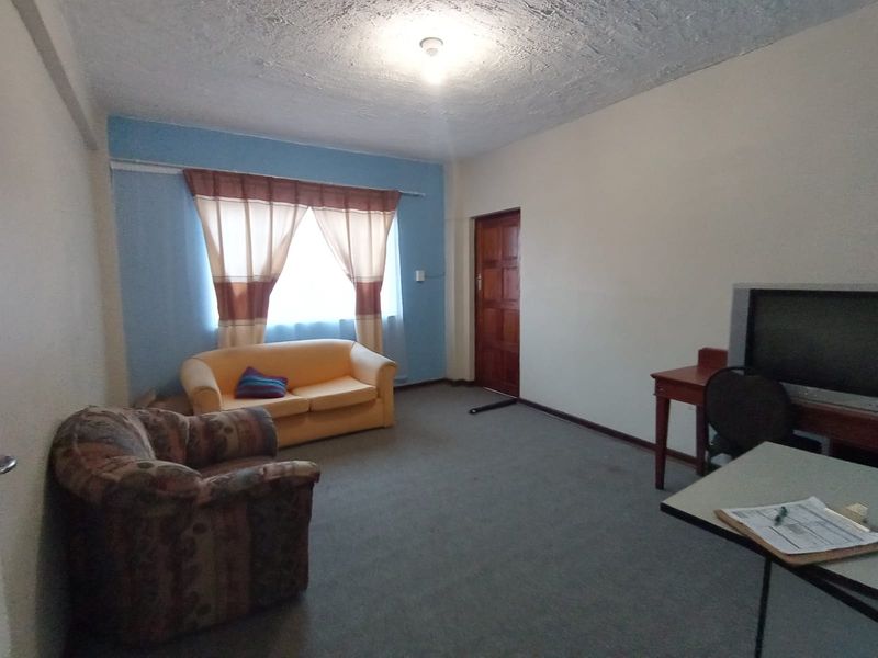 A living room featuring carpet flooring, a textured ceiling, and a timber door, offering a functional space with potential for modernization.