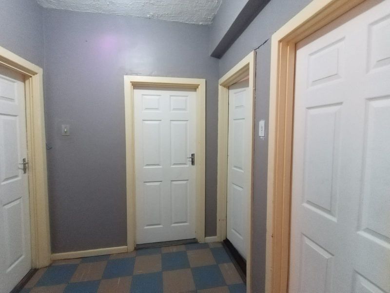 A functional hallway featuring multiple panelled interior doors, checkered floor tiling, and grey painted walls with some visible plaster cracking.