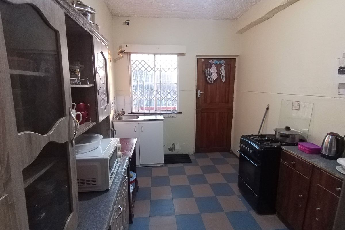 A functional kitchen featuring built-in cabinetry, a stainless steel sink, and a freestanding stove, with tiled flooring and a security gate on the window.