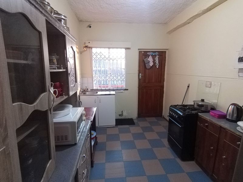 A functional kitchen featuring built-in cabinetry, a stainless steel sink, and a freestanding stove, with tiled flooring and a security gate on the window.