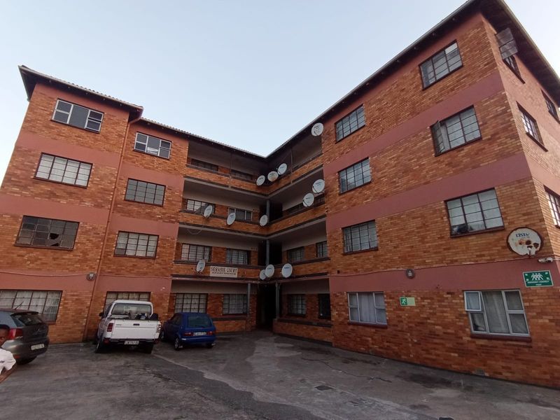 Exterior view of a multi-story brick apartment building featuring steel-framed windows and a paved courtyard area.