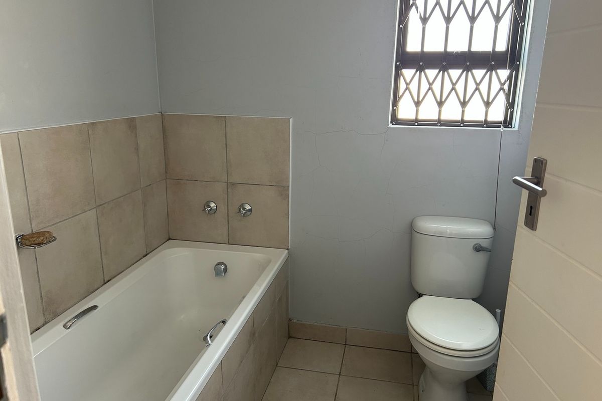 A functional bathroom featuring a bathtub, toilet, and tiled finishes, requiring minor cosmetic repairs to the wall plaster.