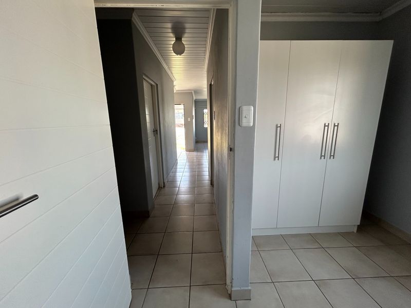 A bright hallway featuring tiled flooring, built-in storage cupboards, and a tongue and groove ceiling, providing access to multiple rooms.