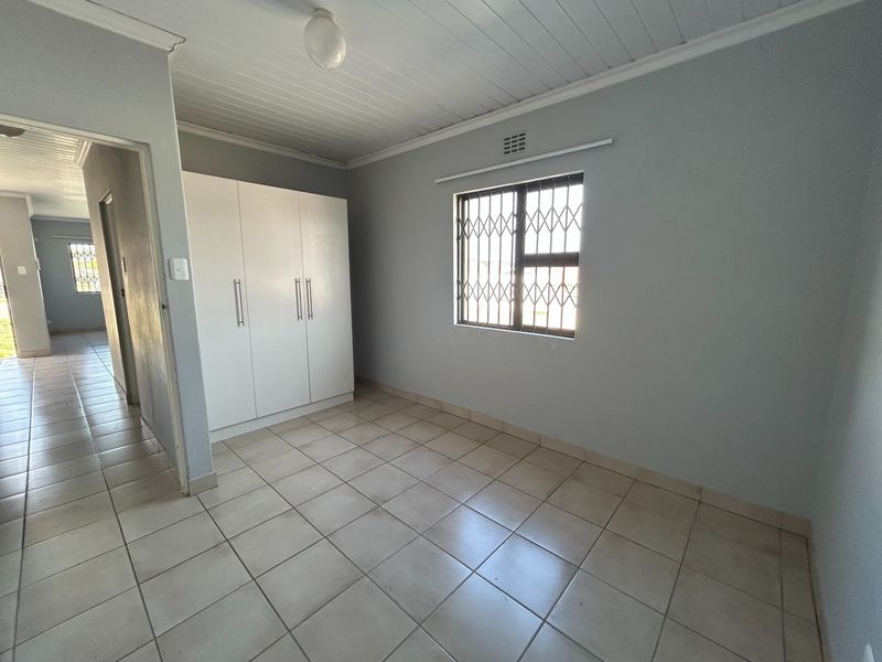 A clean, empty bedroom featuring tiled flooring, a built-in wardrobe, and a window fitted with a security gate.