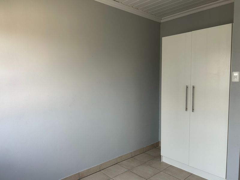 A clean, empty bedroom featuring neutral grey walls, tiled flooring, and a modern white built-in wardrobe with sleek handles.