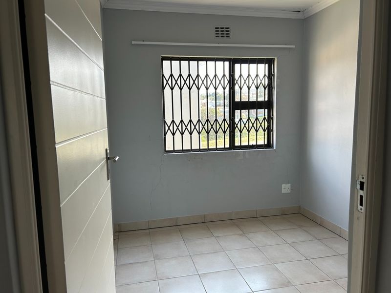 An empty bedroom featuring tiled flooring, a security gate on the window, and visible wall cracks requiring maintenance.
