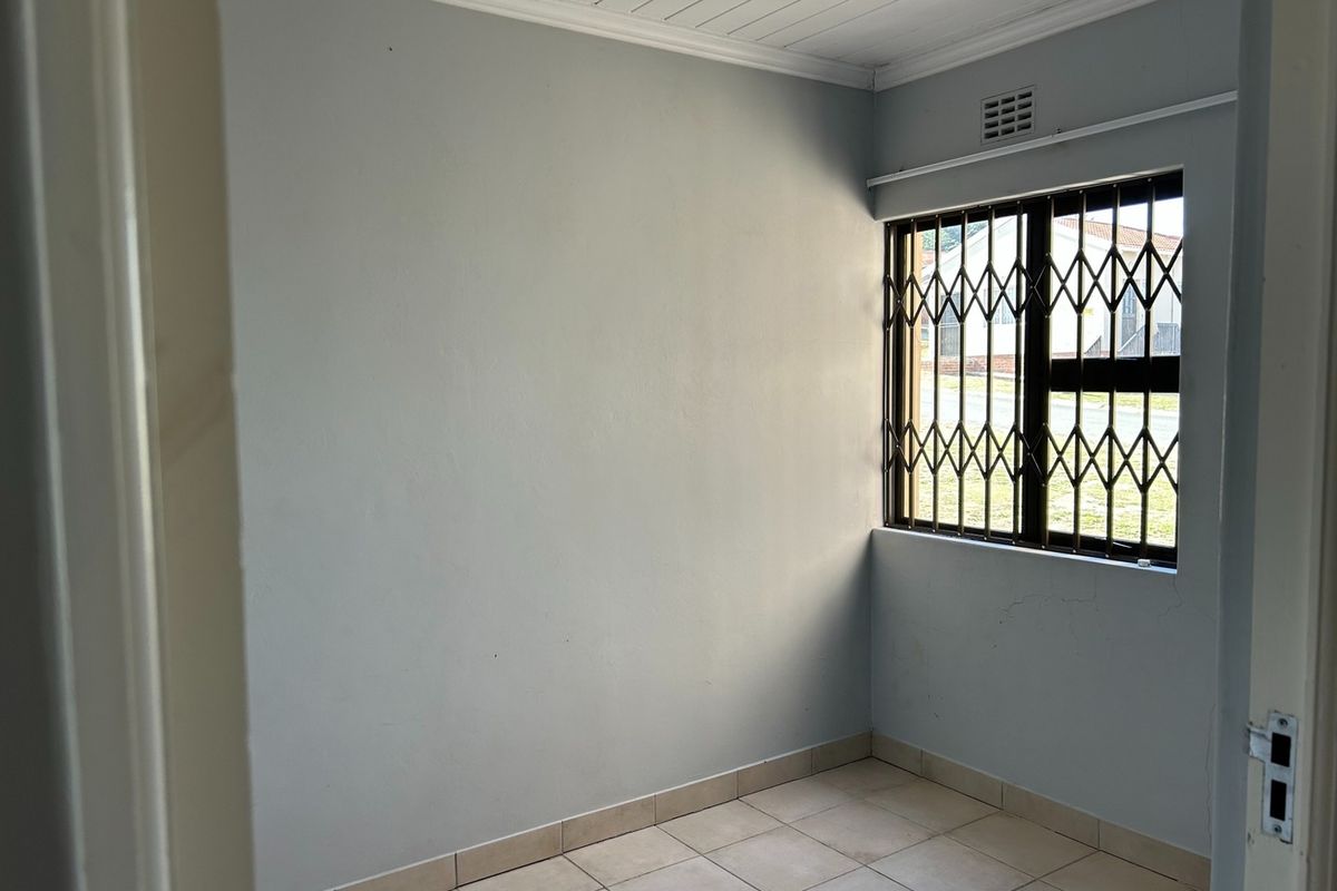 An empty bedroom featuring tiled flooring, a security gate on the window, and neutral wall finishes.