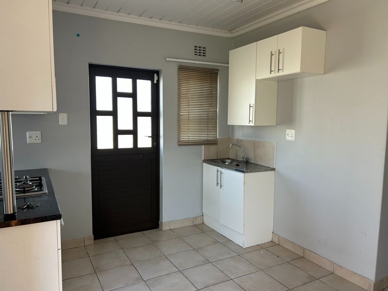 A functional kitchen area featuring built-in cabinetry, a stainless steel sink, gas hob, and tiled flooring with direct access to the exterior.
