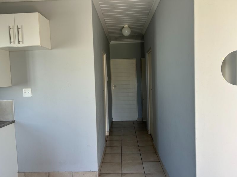 A clean, neutral-toned hallway featuring tiled flooring and a tongue and groove ceiling, providing access to multiple rooms within the home.