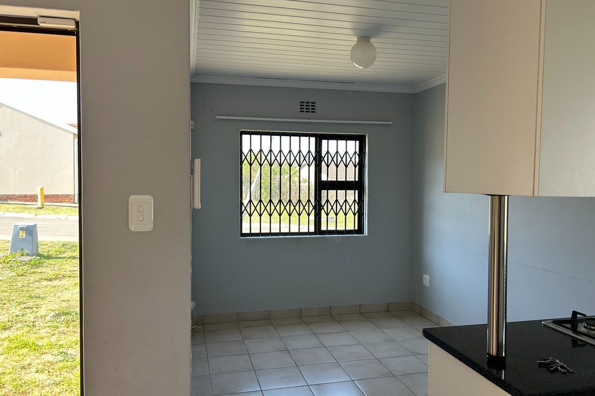 A bright, empty kitchen area featuring tiled floors, built-in cabinetry with granite countertops, a gas hob, and a security-gated window.