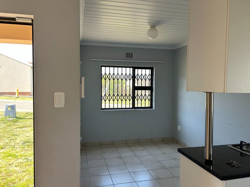 A bright, empty kitchen area featuring tiled floors, built-in cabinetry with granite countertops, a gas hob, and a security-gated window.