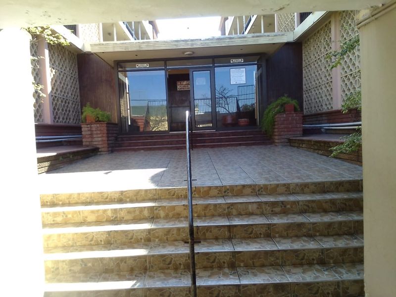 Entrance area of the apartment building featuring a tiled staircase with a metal handrail, glass doors, and decorative brickwork.