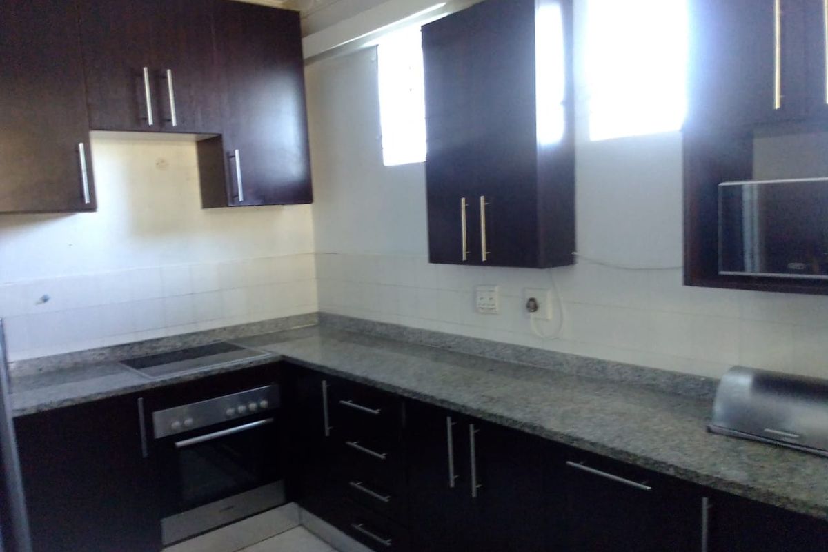 A functional kitchen featuring dark wood cabinetry, granite countertops, a built-in oven, and an electric hob with a tiled backsplash.