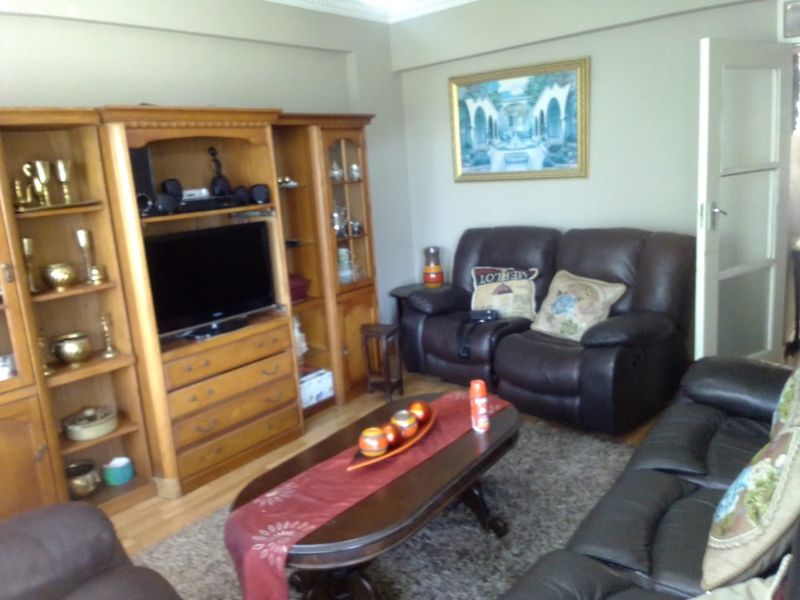 A living room featuring laminate flooring and crown molding, currently furnished with a traditional entertainment unit and leather seating.