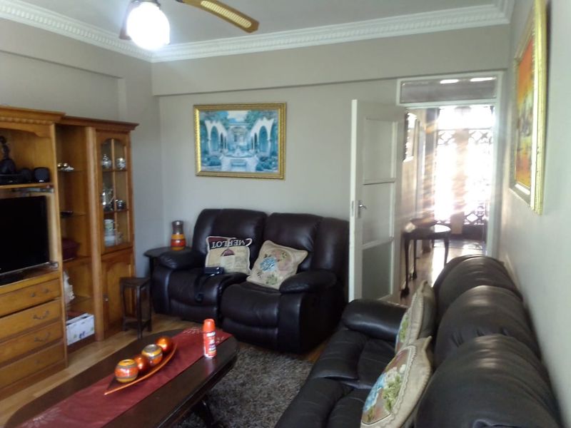 A comfortable living room featuring crown molding, a ceiling fan, and timber flooring, with an open doorway leading to an adjacent hallway.
