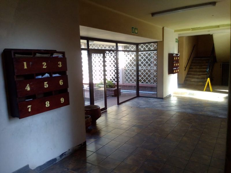 A communal apartment building entrance lobby featuring tiled flooring, wall-mounted wooden mailboxes, and a decorative breeze block screen leading to a staircase.
