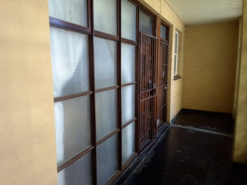 An exterior-facing apartment hallway featuring security gates, timber-framed textured glass panels, and painted concrete flooring.