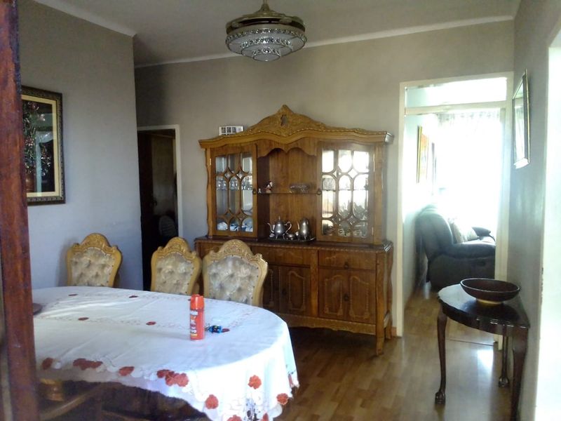 A dining room featuring laminate flooring and a central ceiling light fixture, with an open doorway leading to an adjacent living area.