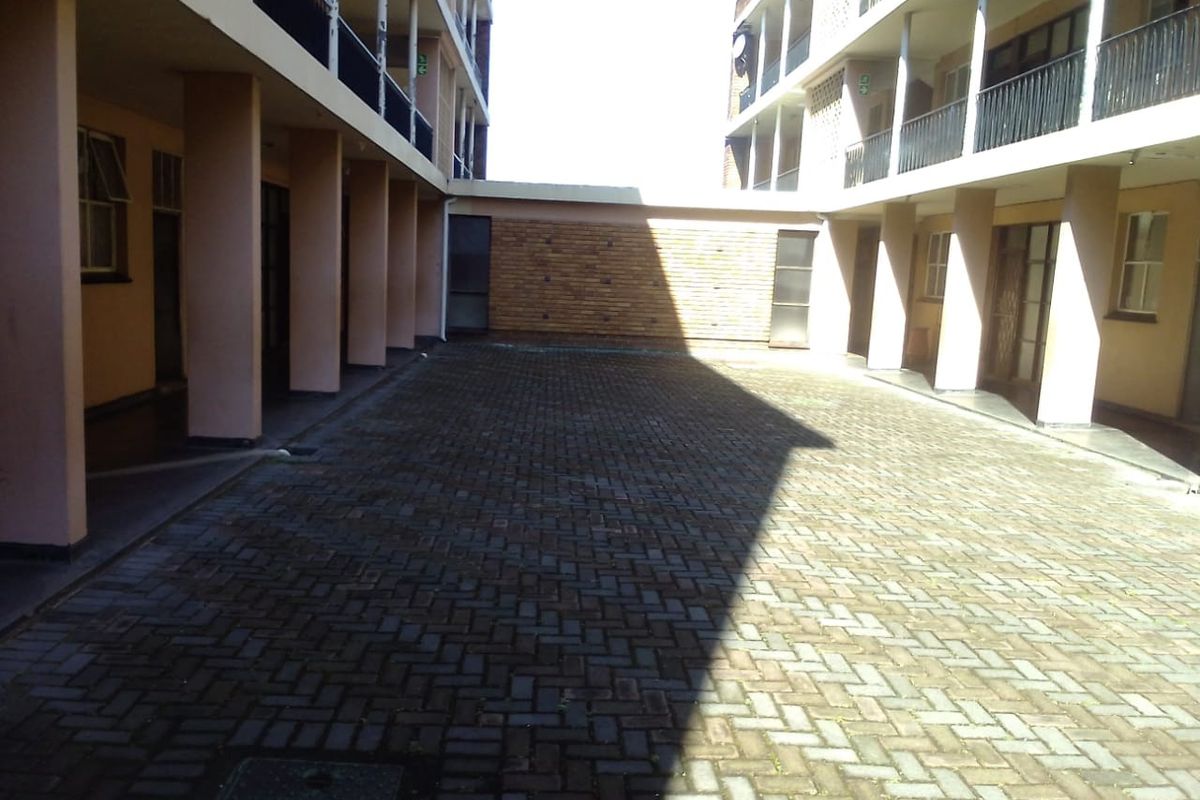 A paved communal courtyard area situated between apartment building wings, featuring brick wall detailing and covered walkways.