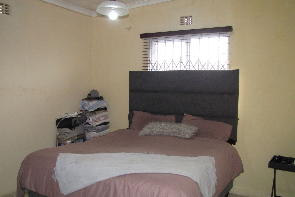 A bedroom featuring a window with security gate and venetian blinds, requiring cosmetic updates to the wall finishes.